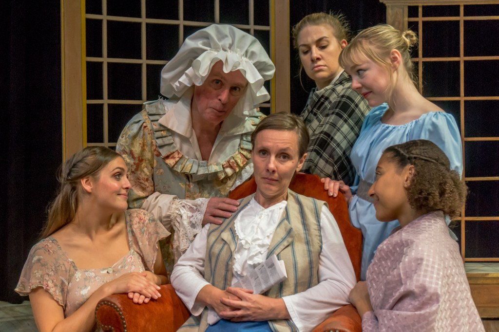 A cast photo from Lost Nation Theater's production of Pride & Prejudice. The patriarch of the Bennet family is seated, surrounded by his wife and four daughters.